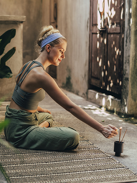 Mujer haciendo yoga y encendiendo unas varas de incienso
